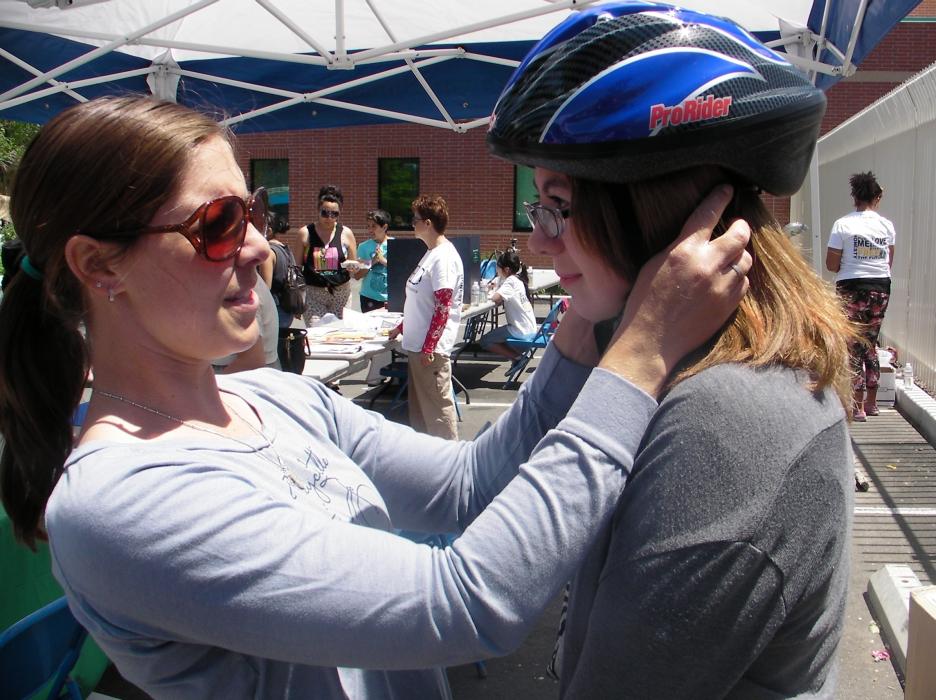 Cortney Bloomer, left, helps Emily Gomer try on a bicycle helmet. More than 60 were given free at Saturday's event.