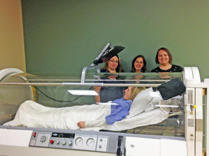 Stacy Martin, Jessica Midlow, and Melissa Vodicka demonstrate how to use the new hyperbaric oxygen chamber with Victoria Stone.
