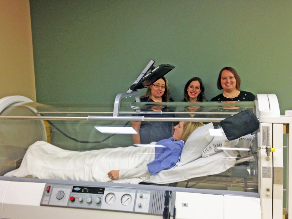 Stacy Martin, Jessica Midlow, and Melissa Vodicka demonstrate how to use the new hyperbaric oxygen chamber with Victoria Stone.