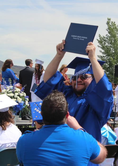 A graduate holds up his diploma for his family to see.