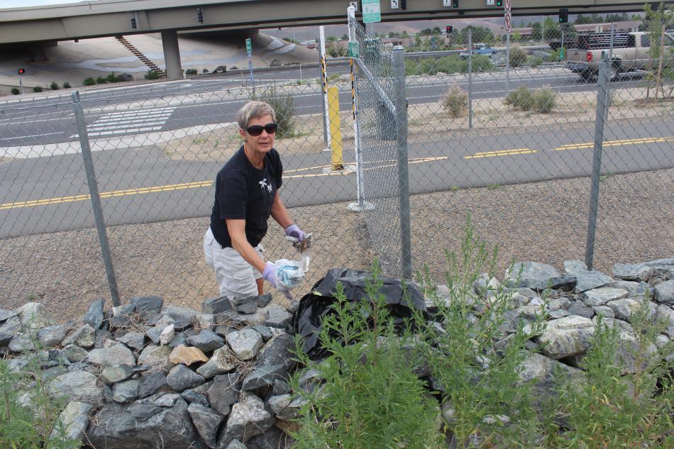 Paula Baum, a trash mob volunteer picks up trash against the fence.