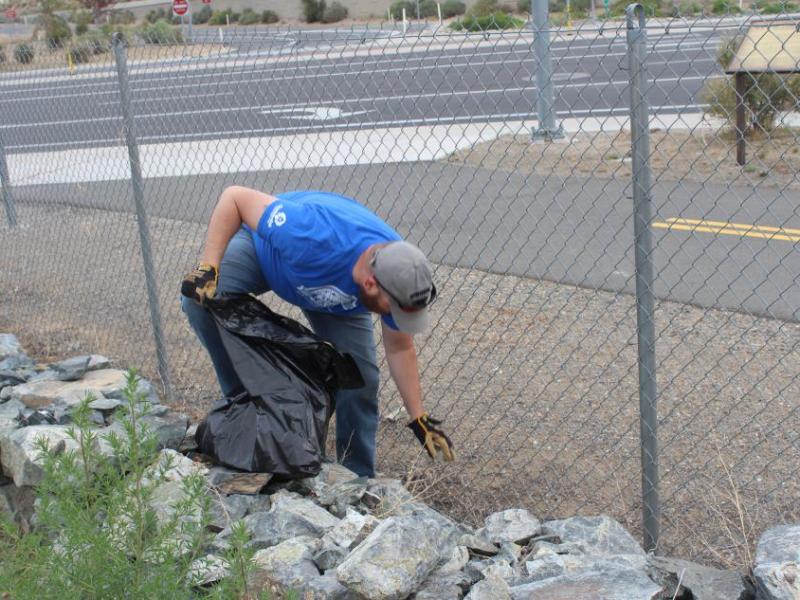 Randy Gaa, a Muscle Power volunteer and organizer of the trash mob picks up trash that has blown against the fence.