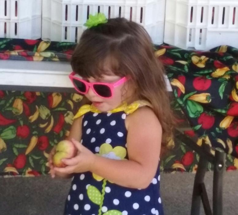Photo by Brett Fisher. Kelissa Ridgel, 2, samples fruit Wednesday along Curry St.