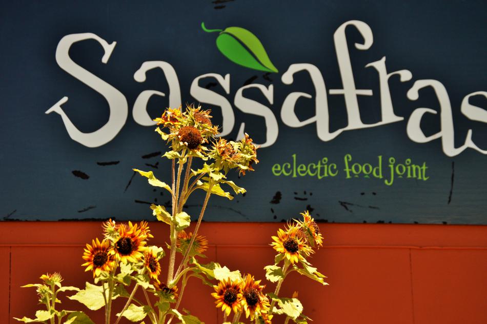 Photo by Brett Fisher. Sassafras Eclectic Food Joint sign framed by sunflowers.