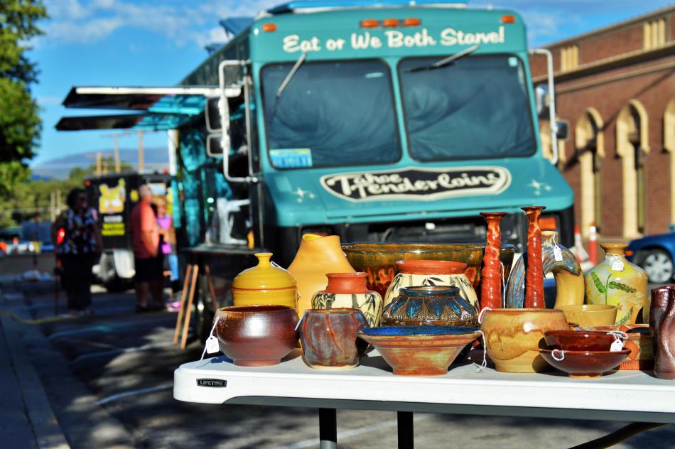 Photo by Brett Fisher. Food truck from Westside Pour House in the background of a table display of pottery.