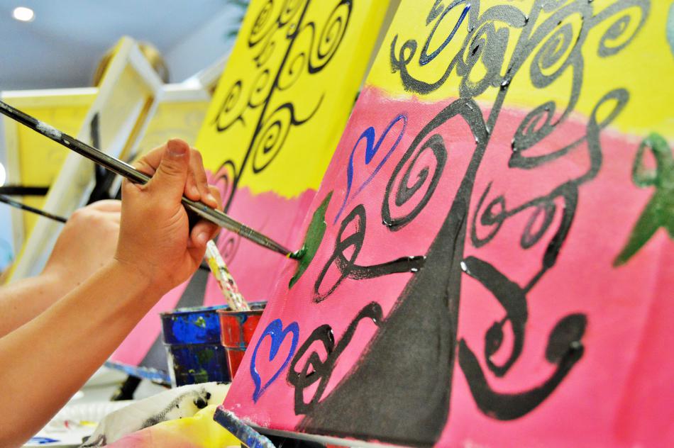 A child applies paint to her canvas painting at Van Gogh and Vino.