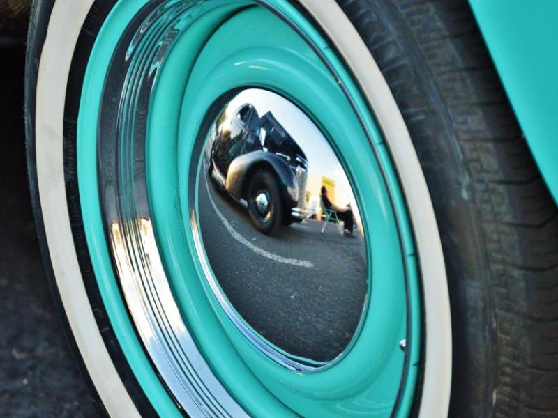 The reflection of a hot rod in the chrome hub cap of a classic Volvo.