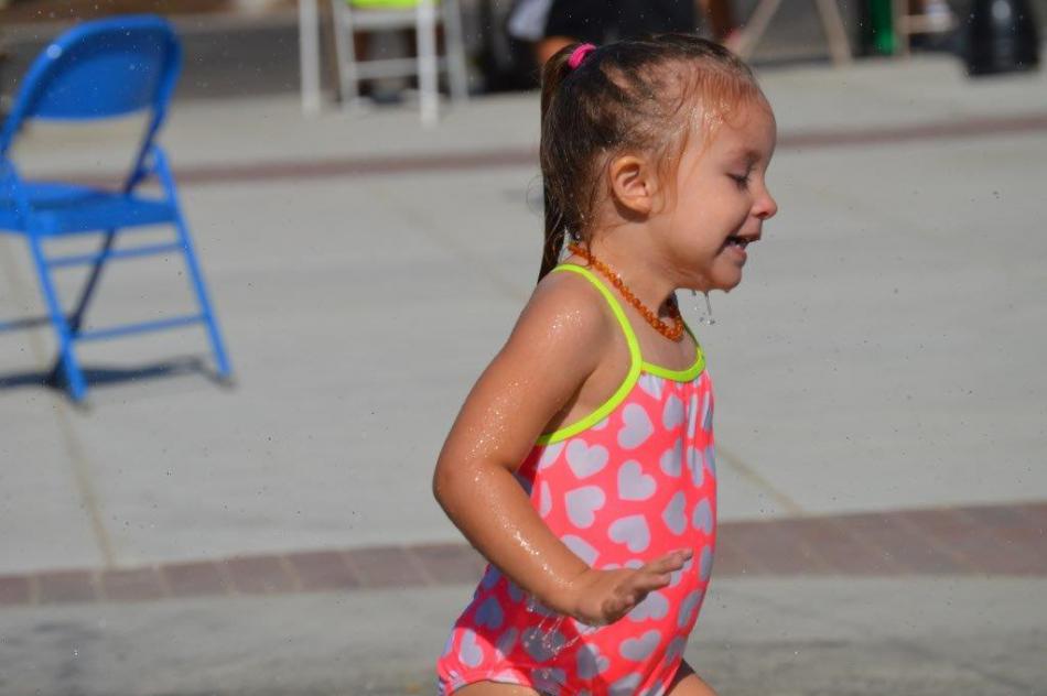 Photo by Lisa Fisher. A girl gets soaked by the splash pad at Bob McFadden Plaza.