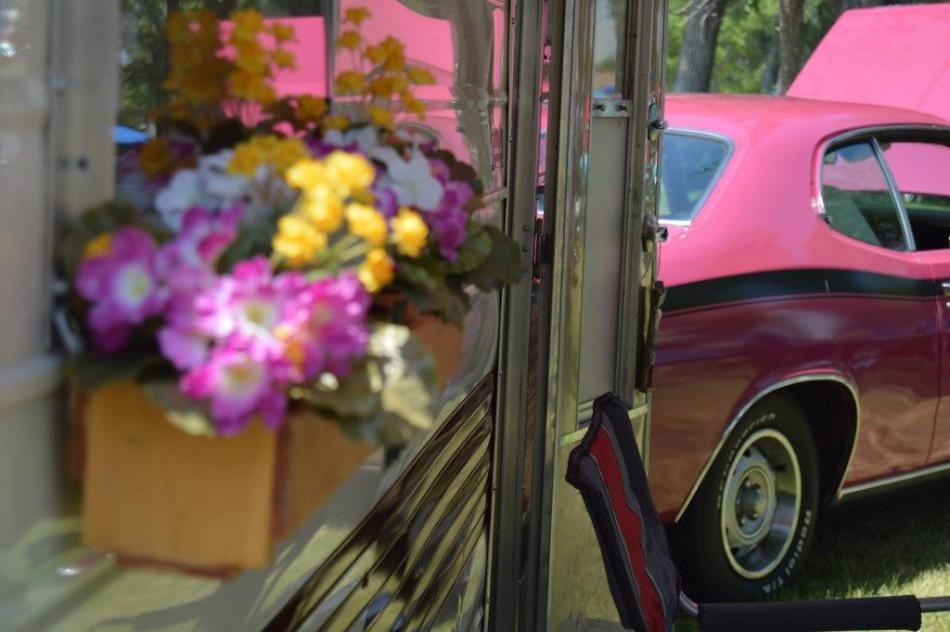 Classic pink automobile pulling at vintage camp trailer.