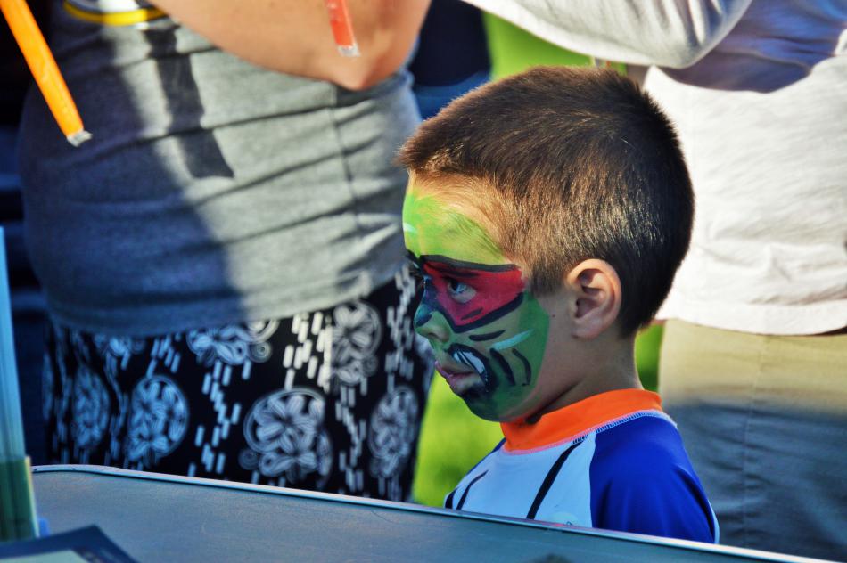 A boy with his face painted watches a puppet show.