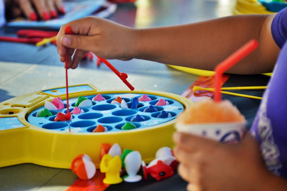 A boy plays a fishing game while holding a snow cone.