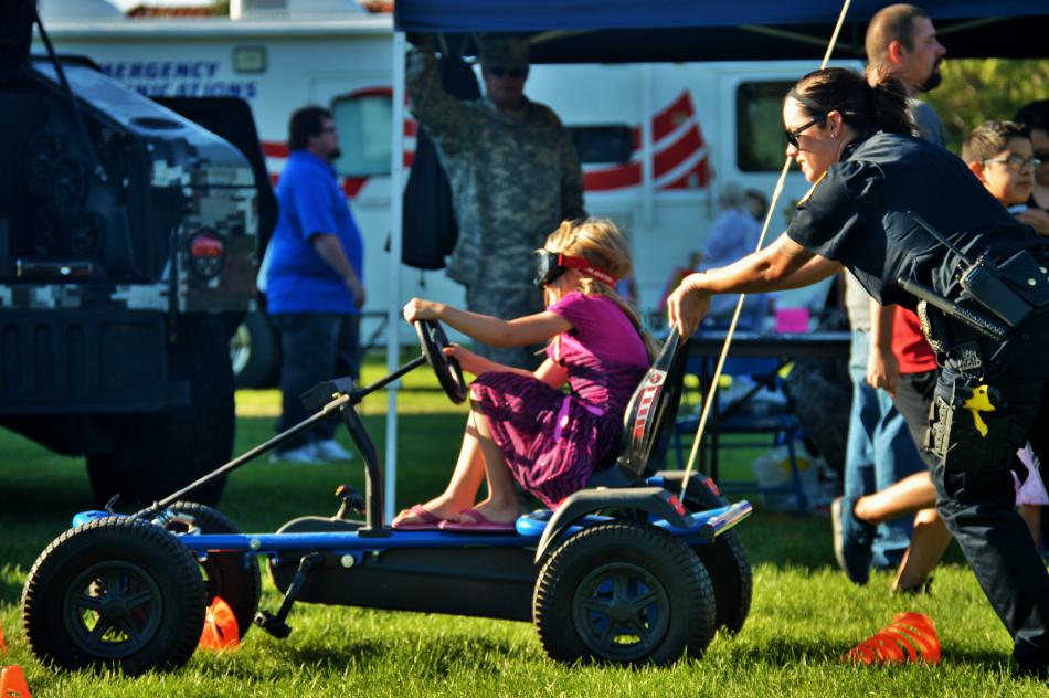An NHP officer pushes a child around a short obstacle course in a go-kart.