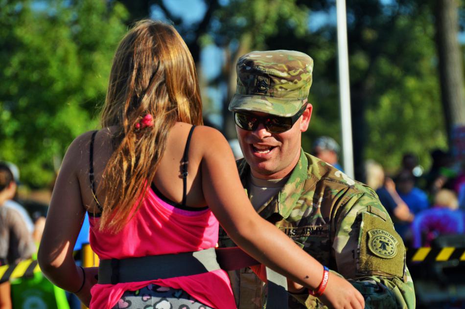 A U.S. Army soldier helps a girl get geared up for the rock climbing wall.