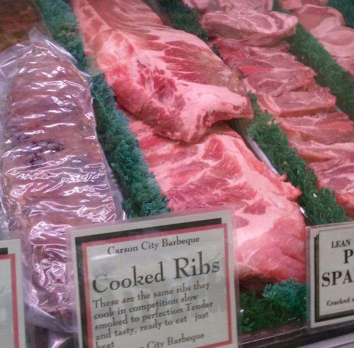 Packaged cooked ribs alongside raw product in the display counter at Butler Meats.