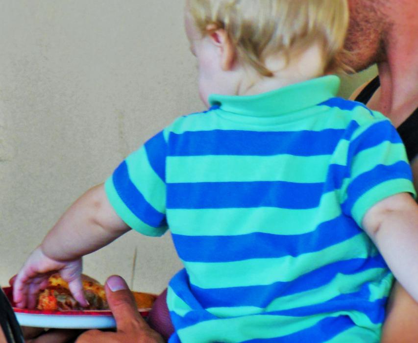 A small boy reaches for a slice of pizza from his dad's plate Wednesday at Papa John's.