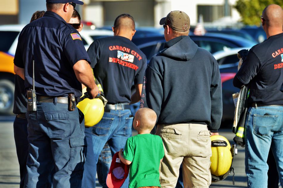 A little boy holds his dad's hand in a group of Carson City firefighters.