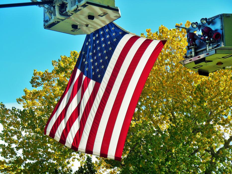 The American flag hoisted by ladders and framed by fall colors.