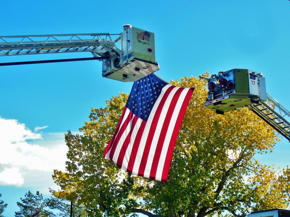 Fall colors accentuate the American flag suspended by two ladder trucks.