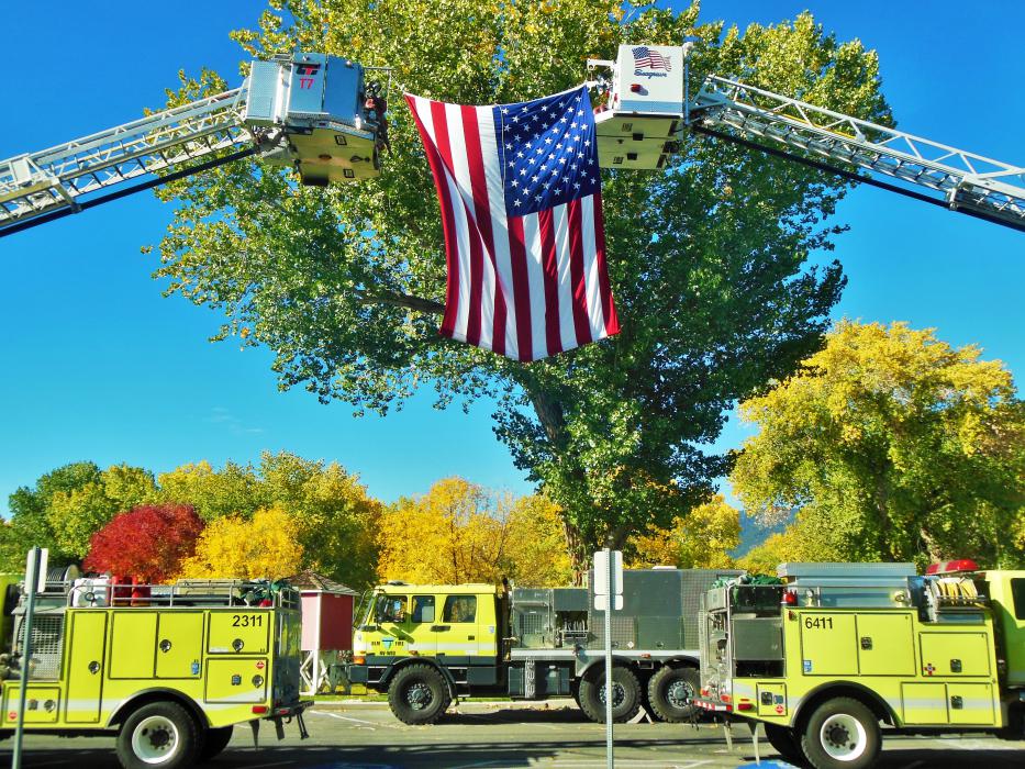 The American flag hoisted by two ladder trucks.