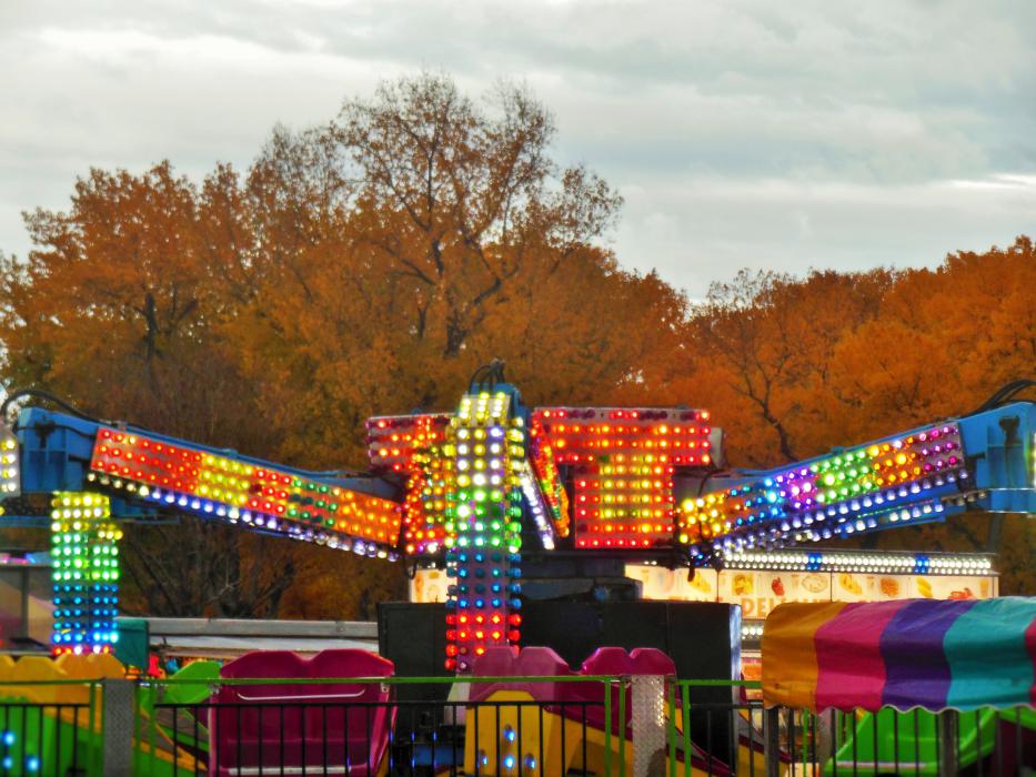 Glowing lights of a ride contrast with the brilliance of fall in the background.