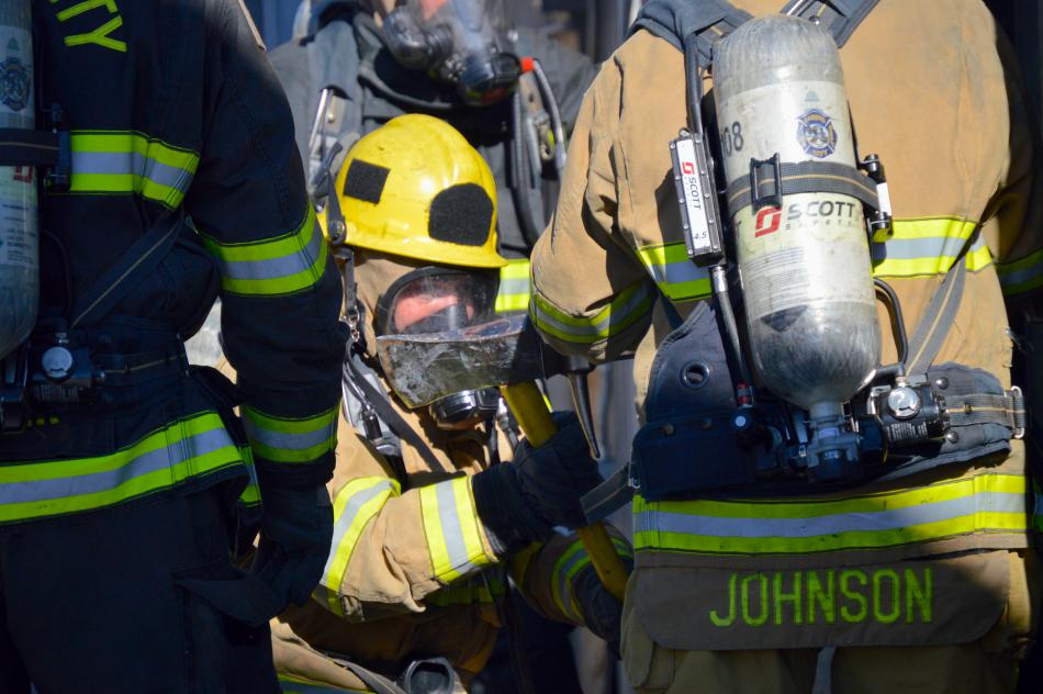 Photos by Brett Fisher. A firefighter uses the blunt end of an axe as a hammer to force open a door.