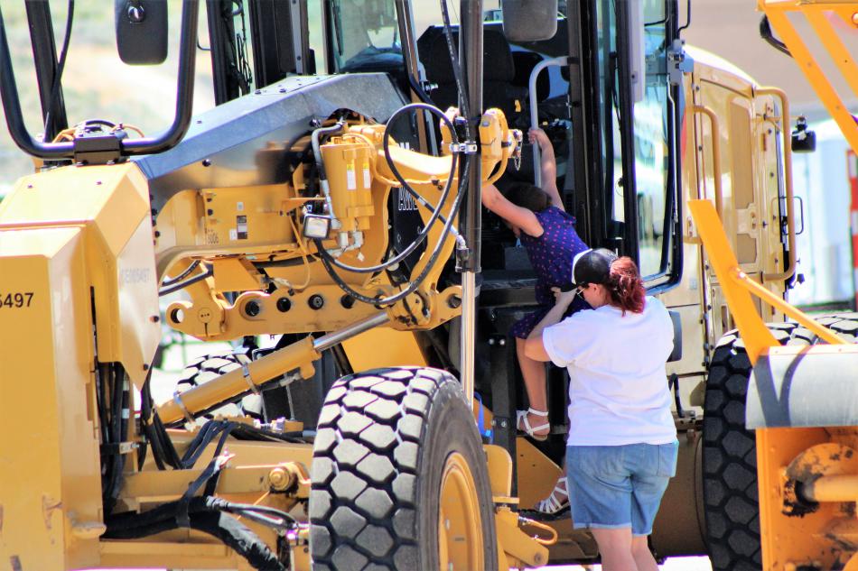 A mother helps her daughter down from the cab of a road grader Saturday.