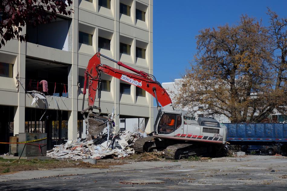 An excavator transfers debris to dumpster after a Bobcat front loader pushes it over the side.