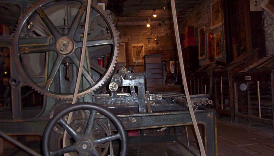 Antique printing press powered by flat-belt, overhead line shaft, at the Territorial Enterprise, Virginia City. Wikipedia photo