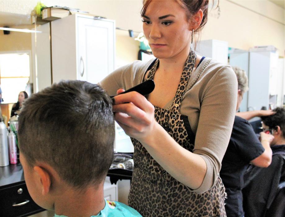A New U stylist cuts the hair of a young customer Saturday as part of a fundraiser for the Schmidt family.