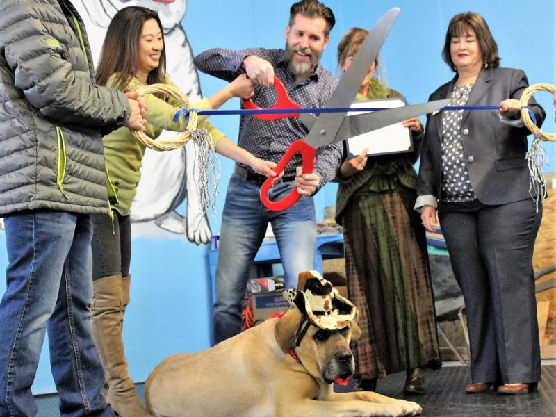 Susan Olson and Phill Kenoyer cut the ribbon Thursday while BooBoo looks on.