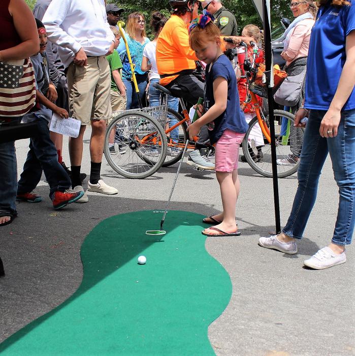 A girls putts a golf ball toward the hole at a booth on East Musser St.