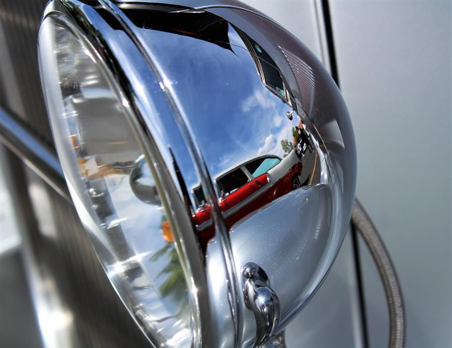 Head lamp of a classic street rod bears the reflection of a Chevrolet Bel Air.
