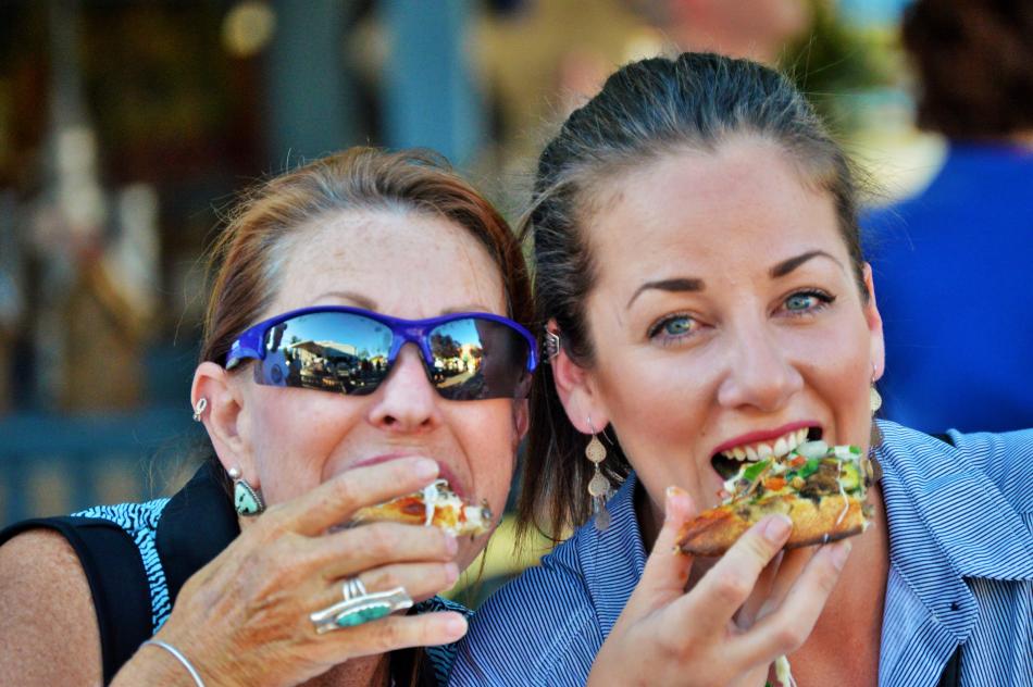 Photos by Brett Fisher. Two ladies bite into pizza during the 2016 Taste of Downtown.