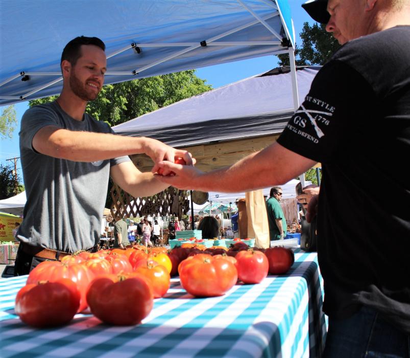 A vendor hands tomatoes to a customer Saturday.