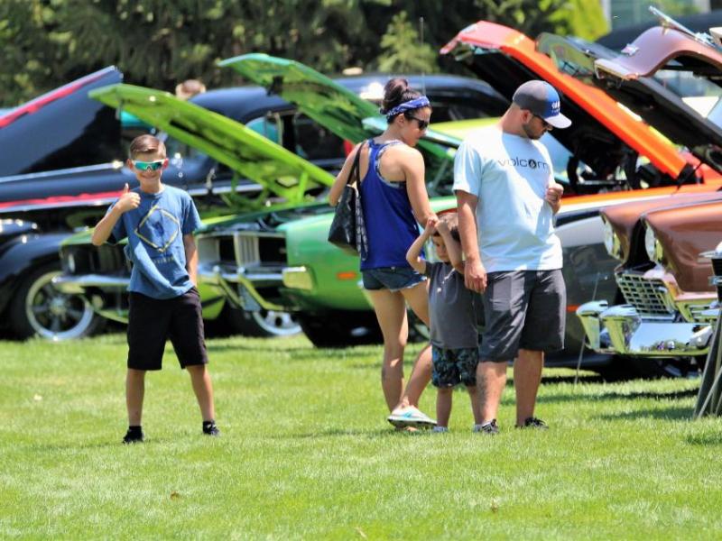 Photos by Brett Fisher. A young man gives a thumbs up to the camera as he and his family view rows of cars.