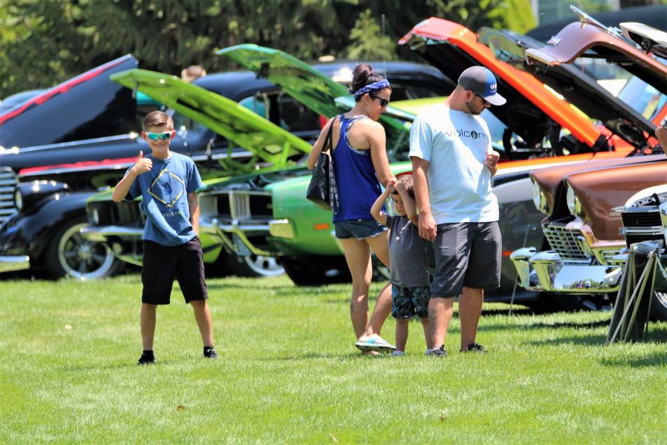 Photos by Brett Fisher. A young man gives a thumbs up to the camera as he and his family view rows of cars.