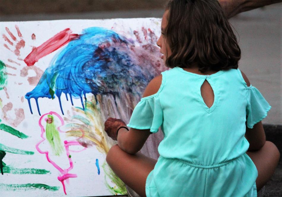 A girl paints a canvas using her hands at the BAC.