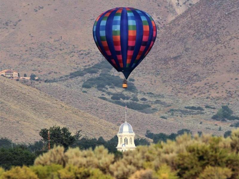 Photo by Brett Fisher. A hot air balloon floats directly above the Nevada State Capitol.