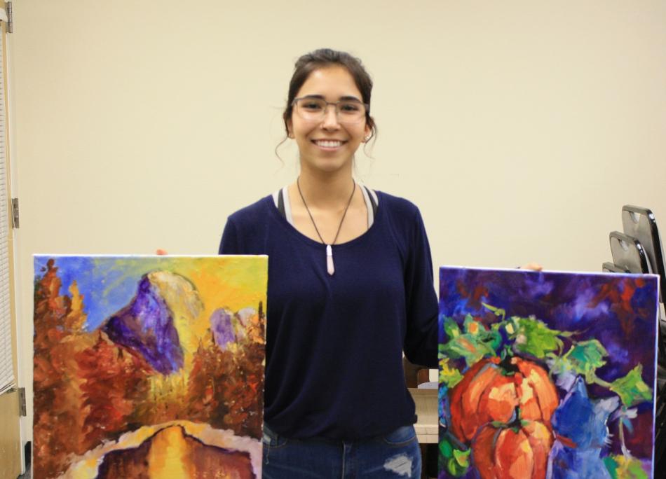 Jazlyn Duran assists with creating art exhibits with paintings donated by artist Carol Benson.