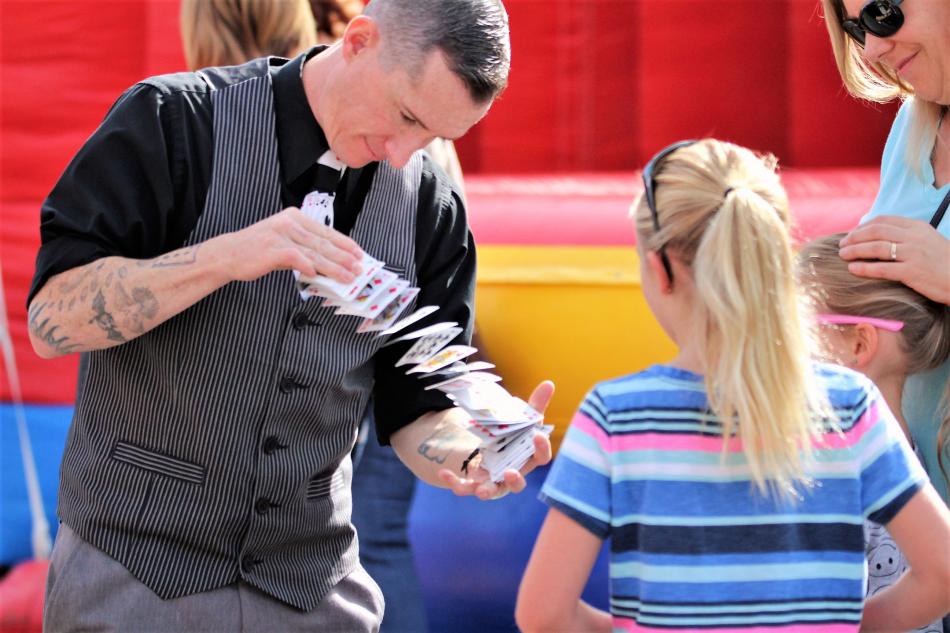 Photos by Brett Fisher. A magician performs card tricks for some young Passport guests Friday.