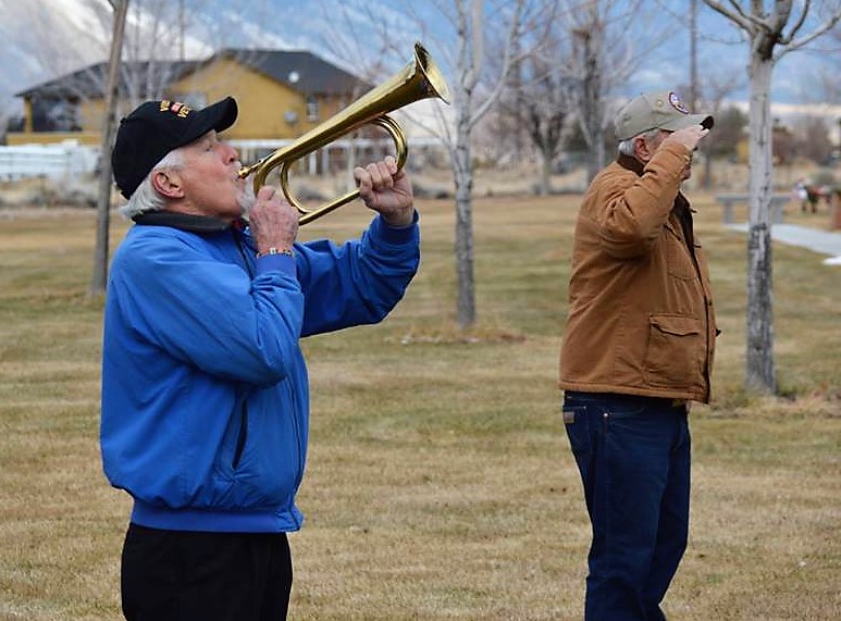 A bugler plays Taps during Saturday's ceremony while a veteran salutes.