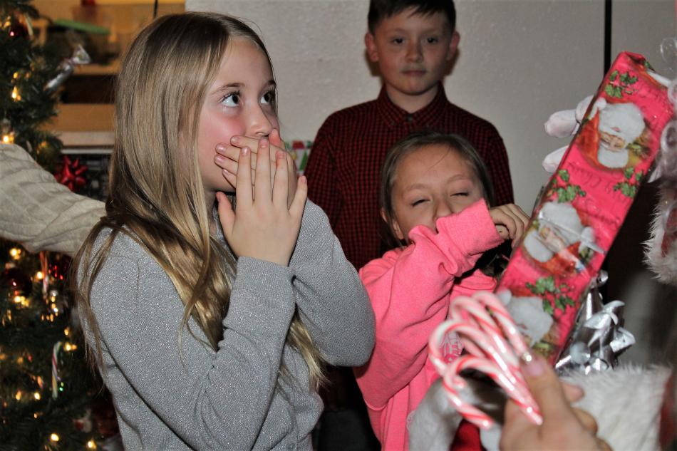 A girl looks completely surprised when Santa hands her a present with her name on it.
