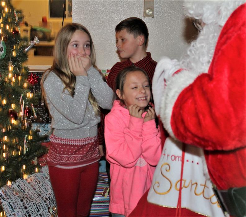 Two girls are excited as Santa Claus opens his sack.