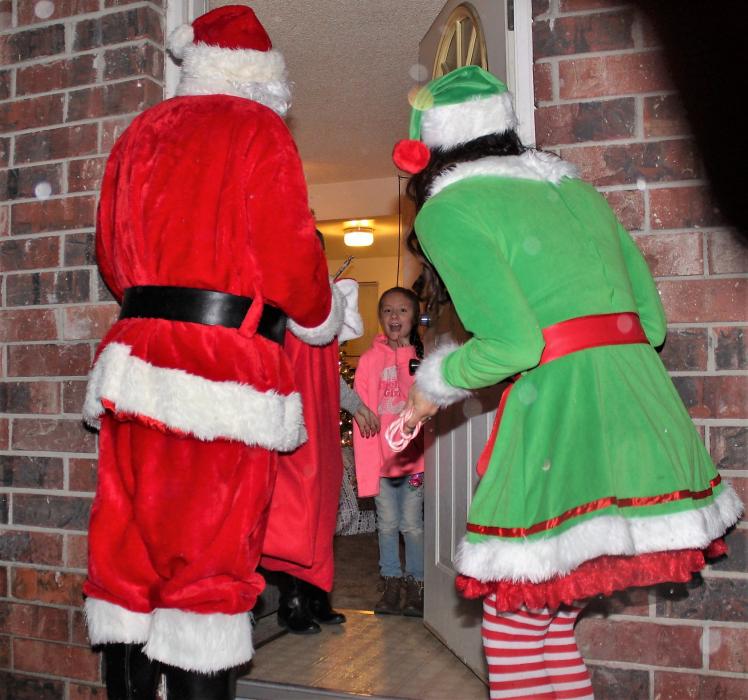 A girl is surprised to see Santa Claus and an elf show up at her front door.