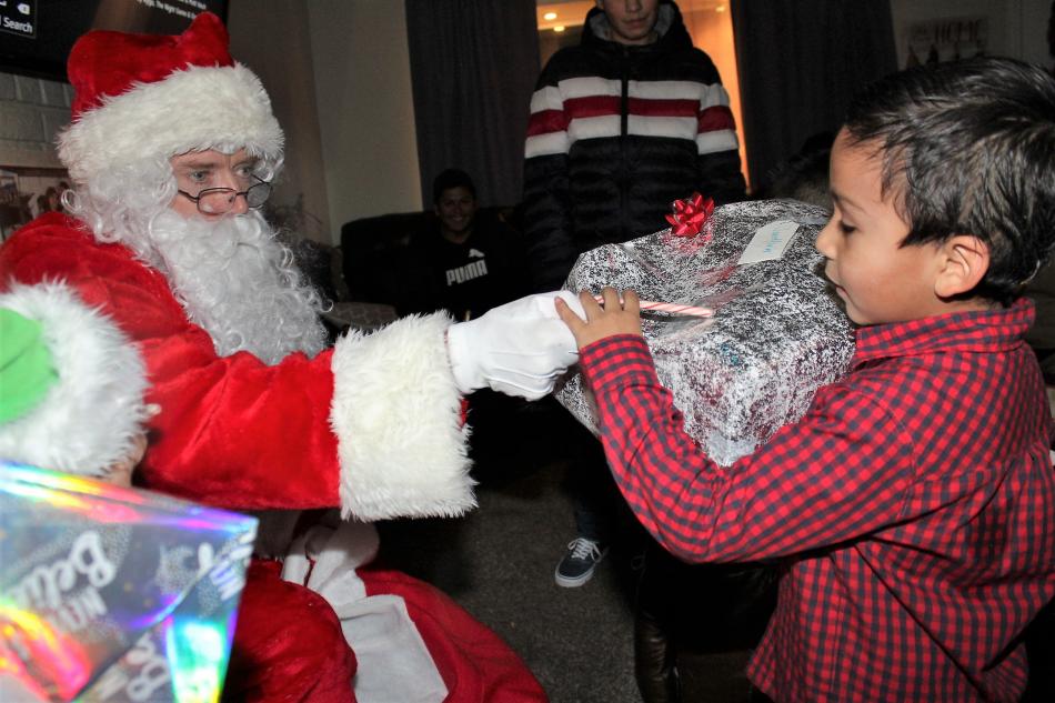 Santa Claus hands a boy his present and a candy cane.