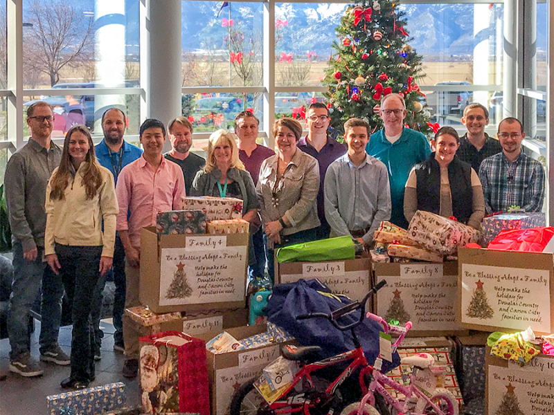A group stands by Christmas gifts near a Christmas tree