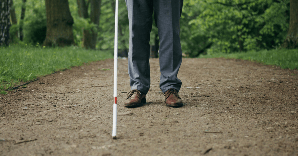 A photo of an individual using a white cane for visual impairment shown from the waist down.