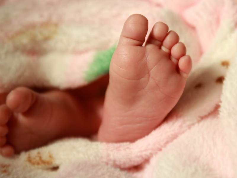 Baby feet poke out from beneath a pink and yellow baby blanket.