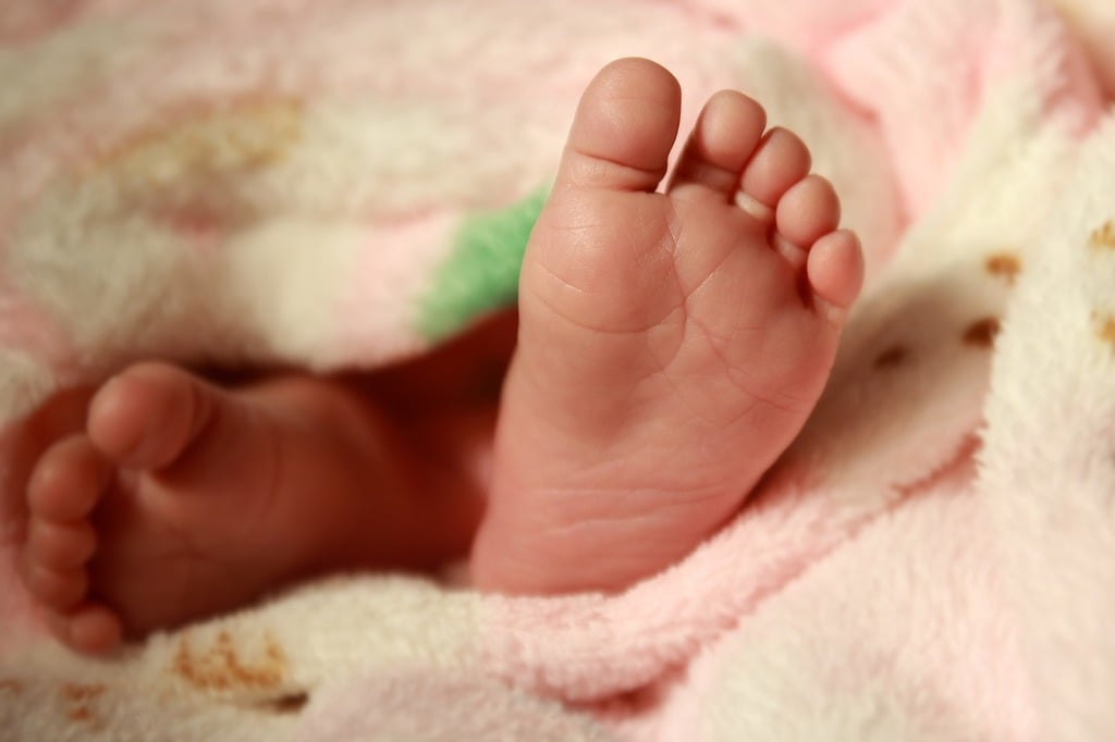 Baby feet poke out from beneath a pink and yellow baby blanket.