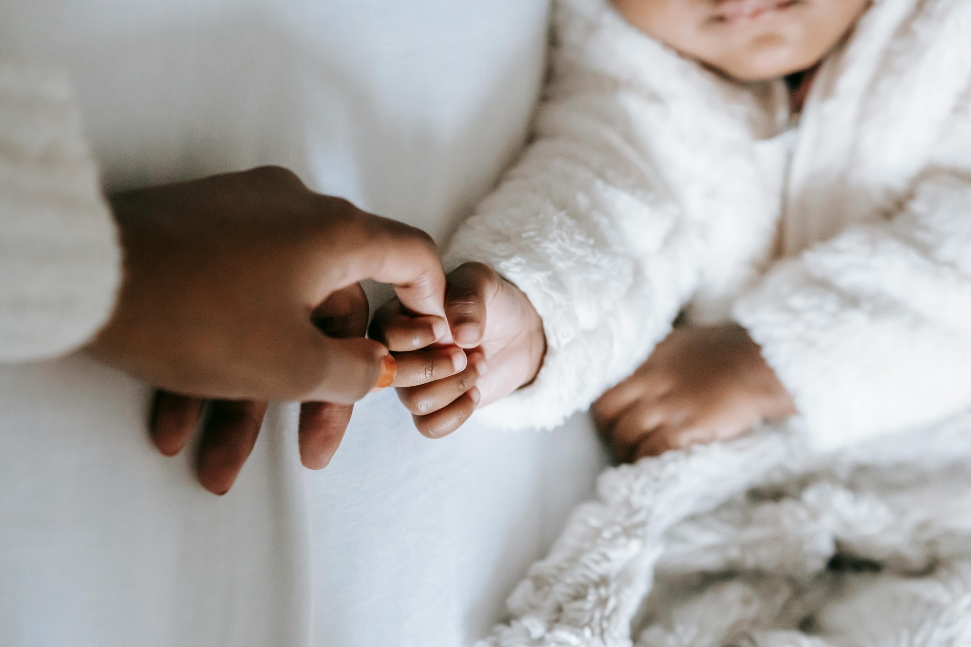 A mother's hand holds a baby's hand against a white backdrop.